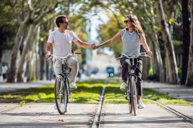 Şehirde el ele tutuşurken bisiklete binen mutlu çiftin fotoğrafı.