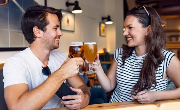 拍了一对年轻漂亮的夫妇 一边喝啤酒一边看着对方的酒吧 图库照片