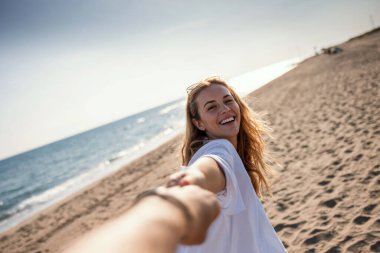 Sahilde el ele tutuşurken günün tadını çıkaran mutlu çiftin fotoğrafı..