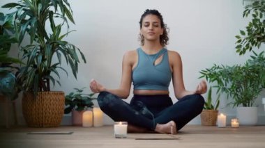 Video of sporty young woman doing yoga and hypopressive exercises while staying in lotus position in living room at home.