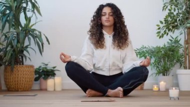 Video of sporty young woman doing yoga and hypopressive exercises while staying in lotus position in living room at home.