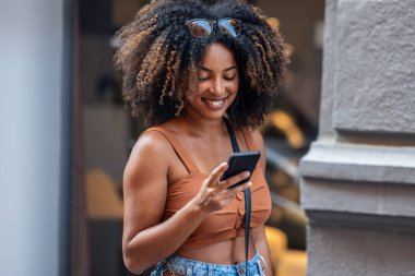 Şehirde alışveriş torbaları taşırken akıllı telefon kullanan gülümseyen kadına yaklaş.