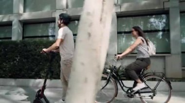 Neşeli bir kadının bisiklet sürdüğü video, şehirde elektrikli scooterlı bir adamla kesişiyor.