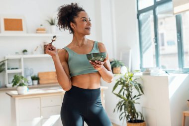 Atletik bir kadının evdeki mutfakta sağlıklı meyve tabağı yemesi.