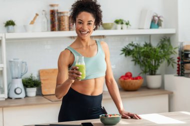 Mutfaktaki kameraya bakarak müzik dinlerken sağlıklı bir smoothie içen güzel, sportif bir kadın..
