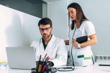 Kendine güvenen kadın ve erkek doktorların tıbbi danışmanlık sırasında dizüstü bilgisayarla konuşmaları ve oynaşmaları..