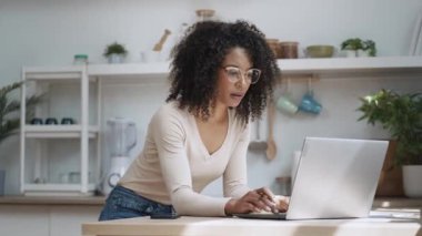 Evdeki mutfakta dizüstü bilgisayarla çalışan kızgın bir kadının videosu..