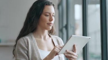 Modern bir ofisteki masada otururken dijital tabletini kullanan bir kadın videosu..