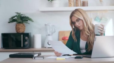 Evdeki mutfakta faturalara ve belgelere bakarken bilgisayarla çalışan güzel bir iş kadınının videosu..