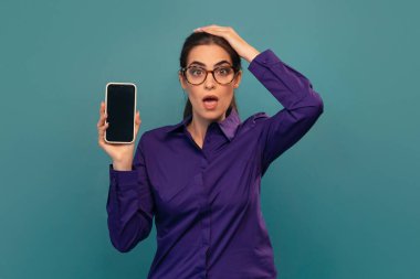 Elinde akıllı bir telefonla kameranın önünde poz veren çekici bir kadının görüntüsü.