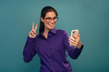 Shot of smiling beautiful woman using her smartphone posing in front of camera on isolated blue clipart