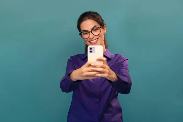 stock image Shot of smiling beautiful woman using her smartphone posing in front of camera on isolated blue