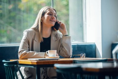 Kahve dükkanında cep telefonuyla mesajlaşan genç bir iş kadınının fotoğrafı.
