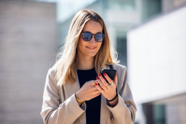 Sokakta yürürken akıllı telefonunu kullanan güzel bir kadının fotoğrafı.