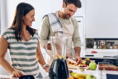 Kocası mutfakta meyve keserken güzel bir kadının blender ile detoks suyu hazırlarken.