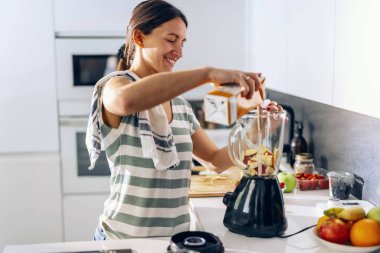 Evdeki mutfakta blender ile detoks suyu hazırlayan neşeli bir kadın.