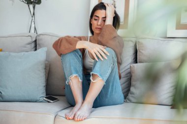 Evdeki kanepede otururken aşırı düşünen depresif bir genç kadın.