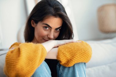 Evdeki kanepede otururken kameraya bakan genç kadının portresi..