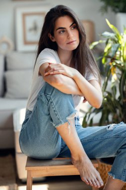 Evdeki oturma odasında kameraya poz veren nazik genç bir kadının portresi..