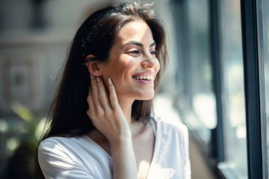 Evdeki oturma odasında kameraya bakarken poz veren gülümseyen genç kadının portresi.