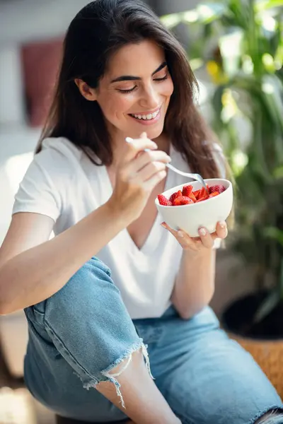 Stock image Portrait of beautiful smiling woman eating healthy strawberries bowl while looking at camera at home.