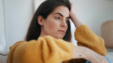 Video of  depressed young woman thinking about her problems while sitting on the sofa at home