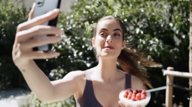 Sağlıklı kahvaltı yapan güzel nüfuzlu bir kadının bahçede akıllı telefonuyla video çektiği bir video.