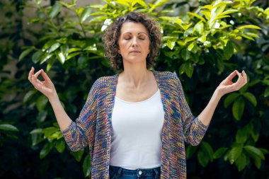 Güzel, olgun bir kadının bahçede yoga ve meditasyon yaptığı bir fotoğraf.