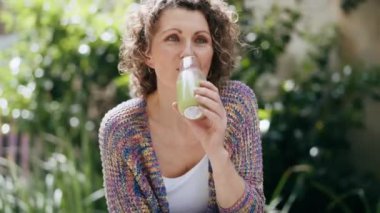 Sağlıklı, olgun bir kadının bahçede detoks suyu içtiği bir video.