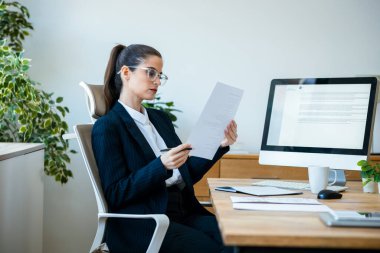 Ofisteki bazı fatura ve belgelere bakarken iş kadınının bilgisayarla çalıştığı fotoğraf