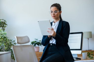 Modern bir ofisteki masada otururken dijital tabletini kullanan bir kadın.