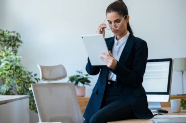 Modern bir ofisteki masada otururken dijital tabletini kullanan bir kadın.