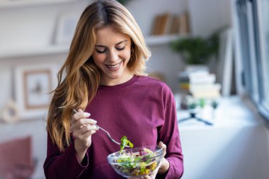 Mutfakta kameraya bakarken sağlıklı salata yiyen güzel bir kadının portresi.
