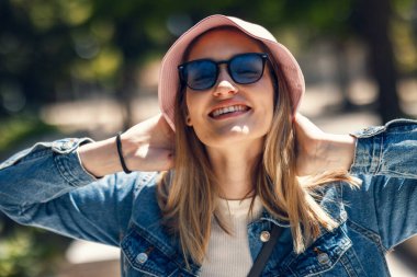 Kameranın önünde güneş gözlüğü ve şapkayla poz veren güzel bir kadın portresi.