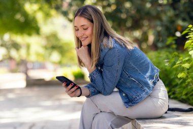 Parktaki bankta otururken güzel bir genç kadının cep telefonunu kullanması..