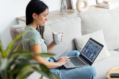 Evdeki kanepede oturup kahve içerken arkadaşlarıyla görüntülü konuşma yapan tatlı bir kadın.