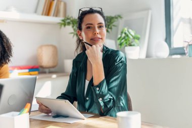 Shot of beautiful business woman working with laptop while looking at camera in a modern startup clipart