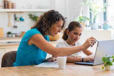 Güzel anne ve kızının evde dizüstü bilgisayarla ev ödevi yaparken çekilmiş bir fotoğrafı.