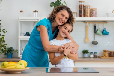 Evdeki mutfakta kameraya bakarken tatlı anne ve kızının kucaklaşması.