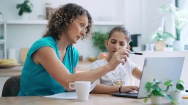 Güzel anne ve kızının evdeki mutfakta dizüstü bilgisayarla ev ödevi yaptığı bir video.