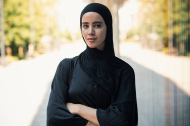 Kentteki kameraya bakan tesettürlü kendine güvenen ciddi bir kadının portresi.