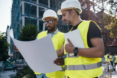Binanın planlarına bakarken kasklı ve kendinden emin iki adamın vurulması. 