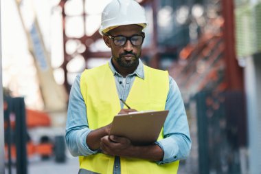 Bir apartman bloğu inşa etmek için gerekli malzemelerin listesini geçen işçi kasklı çekici bir adamın fotoğrafı.