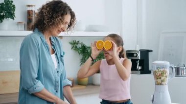Mutfakta kameraya poz verirken annesinin yüzüne portakal dilimleri tutarak eğlendiği küçük mutlu kızın videosu.