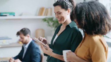 Ofiste dijital tabletini çiğnerken mola veren iki zeki iş kadınının videosu.