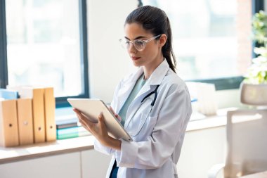 Kadın doktorun muayenede dikilirken dijital tabletini kullanması.