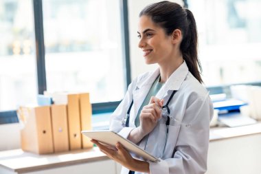 Kadın doktorun muayenede dikilirken dijital tabletini kullanması.