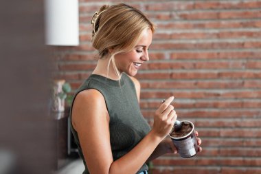 Shot of beautiful young woman eating chocolate ice cream in the kitchen at home  clipart