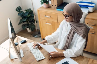 Ofisteki bazı fatura ve belgelere bakarken iş kadınının bilgisayarla çalıştığı fotoğraf