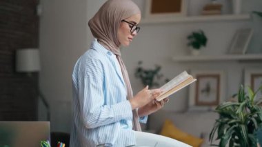 Evdeki oturma odasında kitap okuyan güzel bir genç kadının videosu.